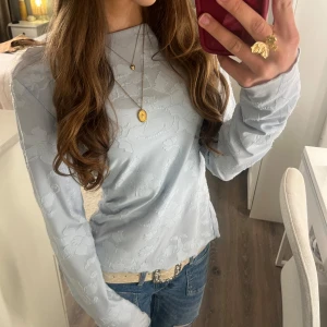 Ljusblå blommig topp från Gina Tricot - Supersöt ljusblå topp från Gina Tricot med diskret blommönster i tyget. Långärmad och i ett tunt, mjukt material som känns skönt mot huden. Älskar den här tröjan den är så somrig och fin💗💗 skriv till mig för fler frågor🫶