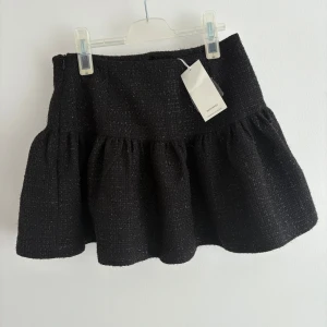 Classy strukturerad volang kjol i svart och silver (nytt skick) storlek M - Perfekt för både vardag och fest! Kjolen är i ett lyxigt tweedliknande tyg som ger en exklusiv känsla och har en volangdetalj. Den är svart med silver glittriga trådar och passar perfekt när man vill klä upp sig mer classy men samtidigt ha fest känsla. Den är aldrig använd då jag köpte fel storlek!