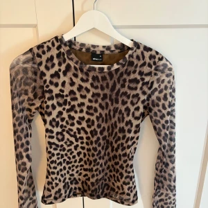 Leopardmönstrad mesh-top Gina Tricot - Säljer en långärmad mesh-top från Gina Tricot i storlek XS. Toppen har ett snyggt leopardmönster i beige och svart, är figurnära och har rund halsringning. Perfekt för dig som vill sticka ut med en trendig look.