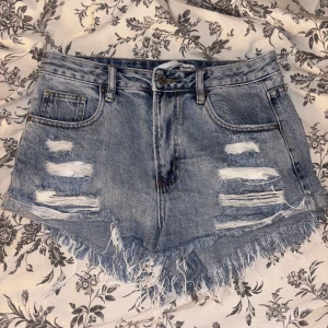 Blå slitna jeansshorts med fransar från laulia  - Snygga blå jeansshorts med slitna detaljer och fransig kant. Klassisk femficksmodell med hög midja och råa kanter för en cool vibe. Perfekta för varma dagar när du vill ha en avslappnad och trendig look.