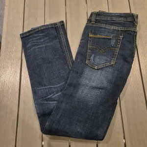 Replay jeans i mörkblå tvätt  - Snygga Replay jeans i mörkblå tvätt med slitningar och kontrastsömmar. Klassisk femficksmodell med guldfärgade detaljer och smal passform. Perfekta för dig som gillar en modern och stilren look.