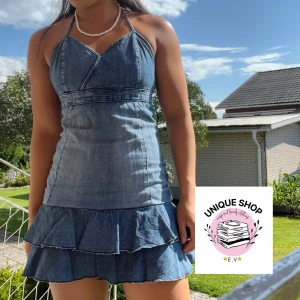 Jeansklänning med volang och öppen rygg - Supersöt kort jeansklänning med volangkjol och omlott-detalj upptill. Klänningen har halterneck, öppen rygg med knyt och sitter figurnära upptill. Perfekt för sommardagar när du vill sticka ut lite extra. OBS: är man lite kortare så kan man vika upp den som på bilden. Klänningen har dragkedja med! MÅTT: 73cm (från byst till slutet)  🫶🏻🫶🏻🫶🏻😍😍😍
