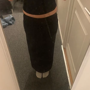 Svart långkjol med slits - Säljer en svart långkjol med tight passform och en slits vid sidan. Jag är 170cm och den passar perfekt. Aldrig använd. Kjolen är ribbad samt har en stilren look som passar perfekt till crop tops eller stickade tröjor. Enkel att styla och superbekväm att bära.