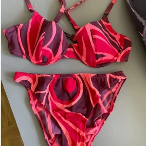 Rosa och vinröd bikini från Change - Snygg bikini från Change med coolt abstrakt mönster i rosa och vinrött. Överdelen har vadderade kupor och justerbara axelband, medan underdelen är klassisk brief-modell. Perfekt för stranden eller poolen, och materialet är mjukt och stretchigt för bästa komfort.