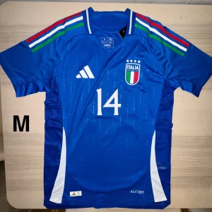 italien landslagströja  Chiesa #14 - Visa ditt stöd för Italien med denna officiella Adidas matchtröja i storlek M! Klassisk blå design med nummer 14 och ITALIA-emblem med fyra stjärnor. HEAT.RDY-teknologi för hög komfort. Helt ny med taggar kvar. Perfekt för match, träning eller som present till en äkta Azzurri-supporter! 💙⚽🇮🇹