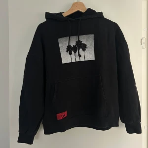 Svart hoodie med palmtryck från pull &bear - Svart hoodie med tryck av palmer i svartvitt framtill. Stor ficka och huva med snörning. 