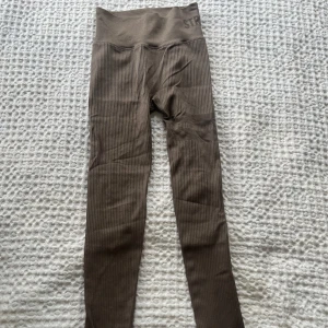 Bruna stronger tights! - Säljer ett par bruna ribbade leggings med hög midja och tight passform från STRONGER. De har diskret struktur i tyget, perfekta för träning eller chill. Materialet är stretchigt och bekvämt, och midjan sitter extra högt för en snygg siluett. NYPRIS 700kr!!