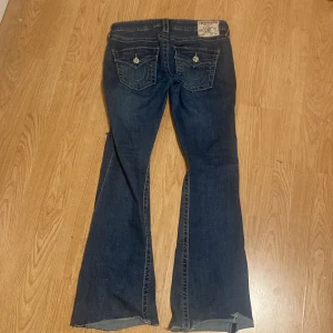 True Religion Joey Low Rise Flare Jeans - Säljer ett par mörkblå True Religion Joey jeans med låg midja och utsvängda ben. Bakfickor med lock och hål. Säljer de pga att de har blivit för små i midjan. Tyvärr så har de gått sönder mellan benen men har sytt ihop det, syns knappt eftersom det är litet och mellan benen. Ett av knapparna på bakfickorna är lite tröga men dom funkar bra! Hade klippt dem eftersom dom hade varit lite för långa för mig som är 163 men längden passar helt perfekt nu! Pris kan diskuteras!❤️❤️ ord pris: 1200-1300 kr