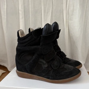 Isabel Marant svarta wedge sneakers - Svarta sneakers från Isabel Marant med cool wedge-sula och kardborreband. Skorna är i mocka och skinn med brun gummisula och hög plös. Perfekta för dig som vill ha en edgy och trendig look med extra höjd. Säljer för det inte kommer till användning. Medföljer 2 dustbags samt kartong. Storlek 39, köpta 2024 använt max 5 gånger. 