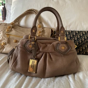 Ljusbrun Q Classic Baby Groove väska! - Köp helst via min vinted för bättre pris @juliavallberg 🤍Snyggaste ljusbruna handväskan i äkta läder från Marc by Marc Jacobs. Den ikoniska modellen Q Classic Baby Groove! En populär och eftertraktad vintagemodell med gulddetaljer och dubbla handtag, långa bandet finns. Väskan är i fint skick men lädret är i vintage skick. Fint skick på gulddetaljerna. Mått: 34x18x12 cm (undersida) Kan hämtas hemma hos mig i Nacka eller skickas 🤍 
