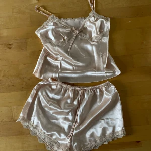 Champagnefärgad satin pyjamas - Snygg champagnefärgad linnetopp och shorts i satin med tunna axelband och spetsdetaljer. Helt ny, aldrig använd. Säljer pågrund av att den inte passade mig💓