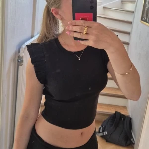 Svart topp med volangärmar - Säljer en svart topp från Zara med ribbad struktur och volangdetaljer på axlarna. Inte använd särskilt mycket, så skicket är väldigt bra! Stl S, men jag upplever den mer som en xs