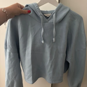 Ljusblå hoodie med huva och snörning - Fin croppad ljusblå hoodie med huva och snörning framtill. Tillverkad i bomullsmaterial. 