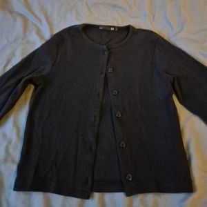 Svart kofta med knappar - En stilren svart kofta från Lager 157 i storlek XS. Koftan har rund halsringning, långa ärmar och knäppning framtill med svarta knappar. Materialet är mjukt och känns som bomull, perfekt att slänga över en t-shirt eller linne.