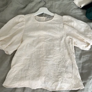 Broderad blus med puffärm från Zara - Superfin ljusbeige blus från Zara med broderade mönster och puffiga korta ärmar. Blusen har rund halsringning och knäppning med knappar i ryggen. Aldrig använd.