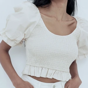 Vit blus med puffärmar från NA-KD - Söt vit blus från NA-KD med puffiga kortärmar och smockad kropp. Toppen har volangkant nedtill och en rundad urringning. Gott skick, använd en gång. (FRAKT INGÅR EJ)