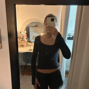 Svart långärmad topp med asymmetrisk ringning - Svart långärmad topp med en snygg asymmetrisk ringning som ger en modern vibe. Tight passform och stretchigt material som sitter skönt på kroppen. Perfekt att styla med både jeans och kjol för en trendig look.