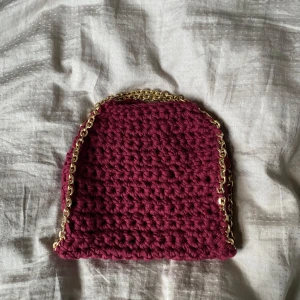 Vinröd virkad axelväska med guldkedja - Superfin vinröd virkad axelväska med chunky guldfärgad kedja som axelrem. Väskan har en mjuk, handgjord känsla och är perfekt för dig som vill ha något unikt och trendigt. Materialet för att göra väskan har kostat 250!!