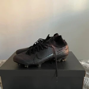 Svarta Nike fotbollsskor med snörning - Snygga svarta fotbollsskor från Nike med diskret glansig finish och klassisk snörning. Skorna har en strumpliknande passform och mönstrad ovandel i syntetmaterial för extra grepp på planen. Storlek 44. Mycket bra skick. 