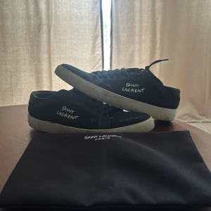 Svarta sneakers från Saint Laurent - Svarta Saint Laurent sneakers med vit broderad logga på sidan och slitna detaljer, skorna är i bra skick men använda därav priset. 