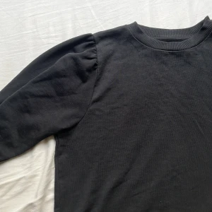 Svart sweatshirt med puffärm - Svart sweatshirt med rund halsringning och snygga puffärmar som ger en trendig siluett. Tröjan är i mjuk bomull och har ribbade muddar vid halsen. Perfekt för dig som gillar en enkel men ändå cool look.