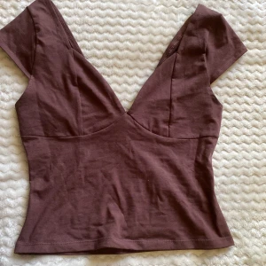 Brun topp från House - Snygg brun croppad topp från House med  v-ringning och korta ärmar. Tillverkad i mjuk bomull som sitter skönt mot kroppen. Perfekt för dig som gillar en enkel men trendig look med lite edge. Aldrig använd och med prislapp kvar.💕