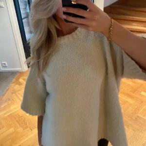 Beige stickad tröja med kort ärm - Supermjuk och oversized beige stickad tröja med korta ärmar och rund halsringning. Perfekt för lager-på-lager och chill dagar. Enkel att matcha med både jeans och kjol för en avslappnad look.