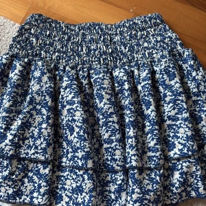 Blåvit blommig kjol - Supersöt blåvit kortkjol från SHEIN med blommigt mönster och smockad midja. Kjolen har volanger och är perfekt för dig som gillar en feminin och somrig stil. Lätt och luftig känsla, passar perfekt till sneakers eller sandaler.