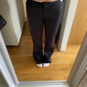 Svarta bootcut kostymbyxor - Snygga svarta kostymbyxor med bootcut-snitt och låg midja. Byxorna har en stilren look med bred linning och dold dragkedja framtill. Perfekta för dig som gillar en klassisk men trendig vibe. Materialet känns mjukt och följsamt.