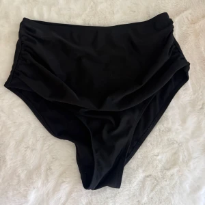 Svarta bikinihöga trosor XL - Snygga svarta bikiniunderdelar med hög midja, tillverkade i mjukt och stretchigt material som sitter bekvämt. Perfekt för dig som vill ha en stilren look på stranden eller vid poolen. Materialet är 82% polyester och 18% spandex för extra komfort.