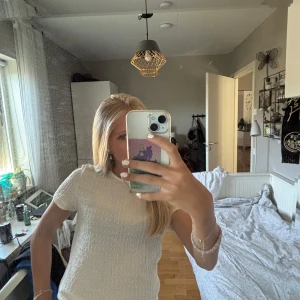 Mönstrad t-shirt - Säljer en vit topp från Vero Moda med korta ärmar och rund hals. Materialet är strukturerat och har en lätt ribbad känsla som ger en cool textur. Perfekt att styla med jeans eller kjol för en fräsch look. Passformen är normal och toppen är enkel men ändå unik.