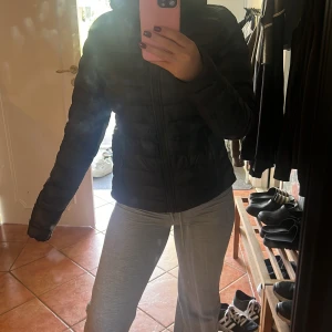 Svart pufferjacka från Everest, strl 38 - Svart pufferjacka från Everest i storlek 38. Jackan har quiltad design, dragkedja framtill och hög krage. Perfekt för kyliga dagar och har en clean, sportig look. Materialet är syntet och jackan är långärmad. Det finns tyvärr en skråma på insidan av jackan. Men inget som syns när den sitter på! 