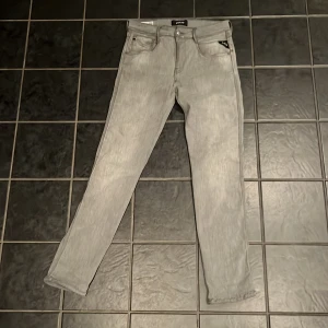 Replay grå jeans slim fit - Snygga grå jeans från Replay i slim fit-modell. Byxorna har klassisk femficksdesign, raka ben och diskreta detaljer på bakfickorna. Materialet är mjukt och stretchigt jeans, perfekt för dig som gillar en modern och stilren look.