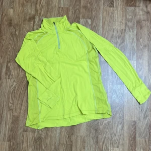 Neongul långärmad träningströja Casall - Neongul långärmad träningströja från Casall med half zip framtill och tumhål vid ärmsluten. Storlek 38. Små fläckar på ena slutet av ärmen (se bild). Använd fåtal gånger.