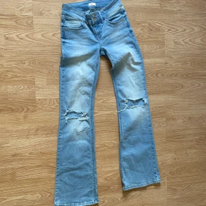 Ljusblå low waist bootcut Jeans från Nelly - Säljer ett par ljusblå jeans low waist bootcut passform och slitna detaljer över knäna. Jeansen har klassiska fickor fram och bak, samt knappar på bakfickorna. Perfekta för en avslappnad och trendig look. Använd 2-3 gånger 