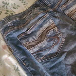 Blå bootcut jeans från EDC by Esprit - Snygga blå jeans med bootcut från EDC by Esprit. De har coola detaljer med bruna sömmar och läderliknande inslag på bakfickorna. Jeansen har normal passform och klassisk femficksdesign. Perfekt för dig som gillar retrovibbar och markerade fickor.