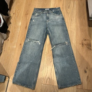Wide jeans från Pull&Bear med slitningar - Säljer ett par blå jeans från Pull&Bear i storlek 38. Modellen är wide med raka ben och slitningar på båda knäna.