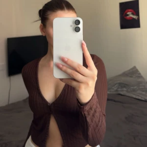 Brun ribbad topp - Säljer en brun croppad kofta från H&M med ribbad struktur och djup v-ringning. Koftan har långa ärmar och två små knappar framtill. Perfekt att styla med höga jeans eller kjol för en chill look.