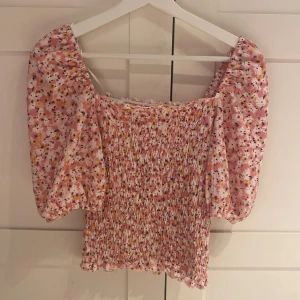 Blommig rosa smockad blus - Supersöt blommig blus i rosa toner med smockad kropp och puffiga korta  armar. 