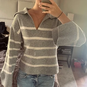 Gråvit randig stickad tröja från Gina Tricot - Supermysig stickad tröja från Gina Tricot i grått och vitt med breda ränder. Tröjan har en krage, v-ringning och långa ärmar med breda muddar. Perfekt för chill dagar men även i skolan och på stan. Snygg till jeans men också kostymbyxor och shorts. Mjuk och skön känsla, loose fit. Kostade ca 600 när den köptes🌸 OBS Alla kläder tvättas innan de skickas