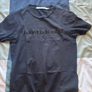 Svart t-shirt Calvin Klein Jeans - Snygg svart t-shirt från Calvin Klein Jeans med stilren logotyp i svart på bröstet. Klassisk rund hals och korta ärmar. Perfekt för dig som gillar enkel och modern design. Materialet är mjuk bomull som känns skönt mot huden.