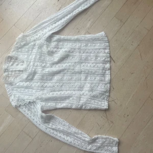 Vit spetsblus med mönster och dragkedja - Supersnygg vit blus i spets med lång ärm och detaljerat mönster med både zigzag och blommor. Blusen har en diskret dragkedja i nacken och är helfodrad med transparenta partier. Perfekt till lite finare tillfället. 