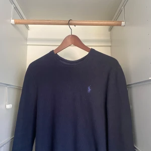 Mörkblå stickad tröja från Polo Ralph Lauren - Säljer en klassisk mörkblå stickad tröja från Polo Ralph Lauren med rund halsringning och broderad logga på bröstet. Tröjan har lång ärm och är perfekt för dig som gillar stilrena och tidlösa plagg. Inga defekter! 