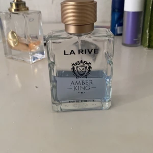 La Rive Amber King Eau de Toilette ungefär 45 ml kvar  - Amber King från La Rive är en eau de toilette i en stilren, fyrkantig glasflaska med guldig spraykork. Flaskan rymmer 100 ml och har en elegant design med svart text och emblem på framsidan. Doften är maskulin och flaskan har en ljusblå vätska. Flaskan rymmer 100 ml ungefär 35/40 ml kvar 