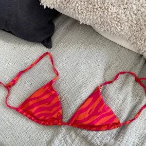 Zebramönstrad bikini i orange och rosa - Snygg trekantsbikini med zebramönster i stark orange och rosa. Bikinin har justerbara axelband och knyt i ryggen