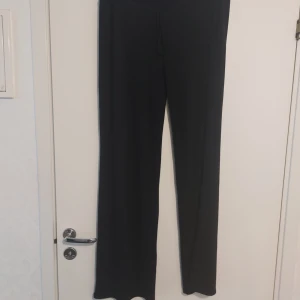 Svarta stickade byxor från Nelly - Svarta mjukisbyxor från Nelly med breda ben och skön passform. Byxorna har snörning i midjan och är gjorda i mjukt bomullsmaterial. Perfekta för chill dagar eller när du vill vara extra bekväm. Stilrena och enkla att matcha med din favorittröja.Slutsålda på sidan.Endast testad.Lappen är bortagen.