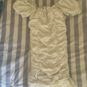 Vit kort klänning med puffärmar - Supersöt vit kort klänning med puffiga kortärmar och broderade detaljer. Klänningen har omlott-snörning vid axlarna och är gjord i mjuk bomull med volangkant. Den är även väldigt stretchig!❤️