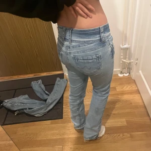 Ljusblå straight jeans med dubbelknapp - Säljer ett par ljusblå pepe jeans, snygga slitningar. Jeansen har låg midja, klassiska fem fickor och stängs med två knappar fram.