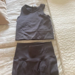 Stronger sett xs  - Säljer en mörkgrå ribbad linnetopp från Stronger i storlek XS. Toppen är ärmlös med breda axelband och har en croppad passform. Materialet är stretchigt och passar perfekt till träning. Diskret Stronger-logga framtill. Säljer även byxorna till💕