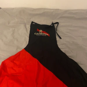 Svart och röd G.H. Mumm köksförekläde - Snygg och unikt köksförekläde från G.H. Mumm Champagne med broderad logga på bröstet. Du blir helt klart en snygging vid grillen!